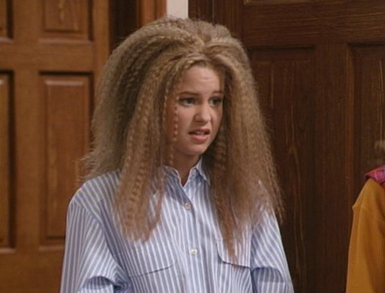 DJ on the TV show Full House with crimped hair. She's wearing a blue and white stripped button down shirt.