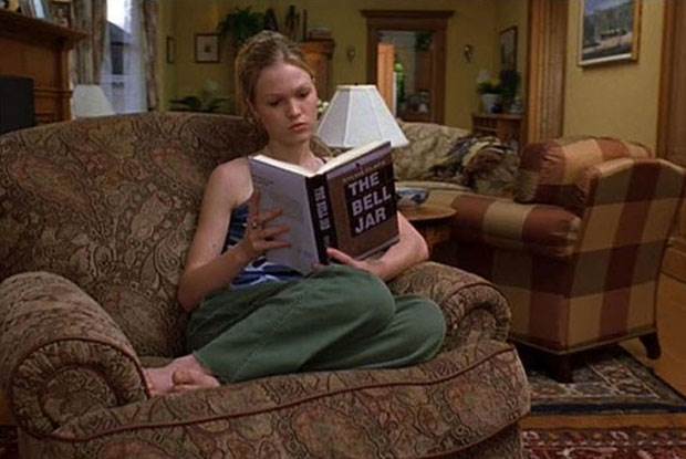 Julia Stiles in the movie 10 Things I Hate About You. Sits with her legs up on an armchair reading a copy of The Bell Jar by Sylvia Plat.