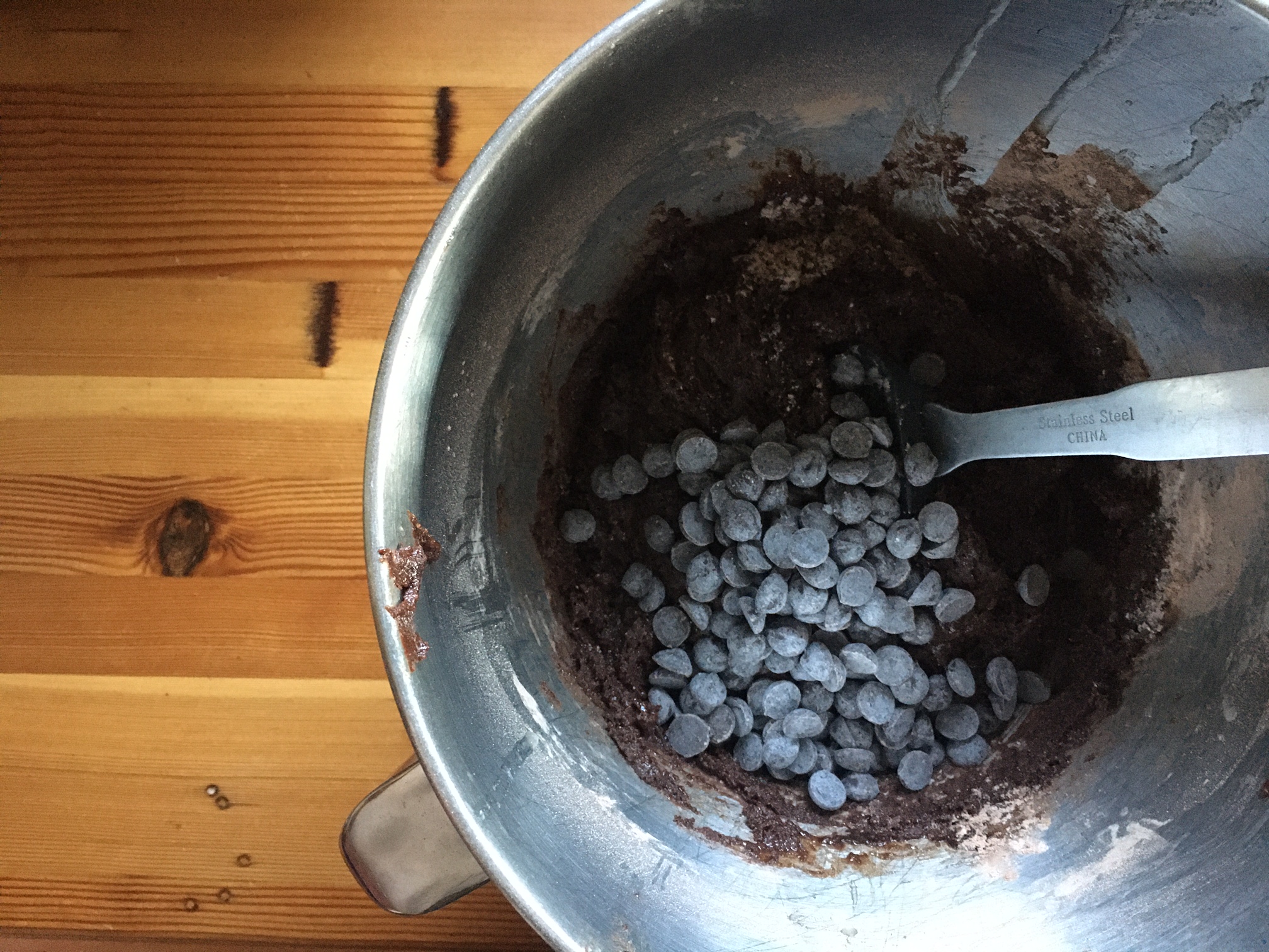 Overhead shot of a mixing bowl on a wood counter top. There's a chocolate batter with chocolate chips waiting to be stirred in with a spatula.