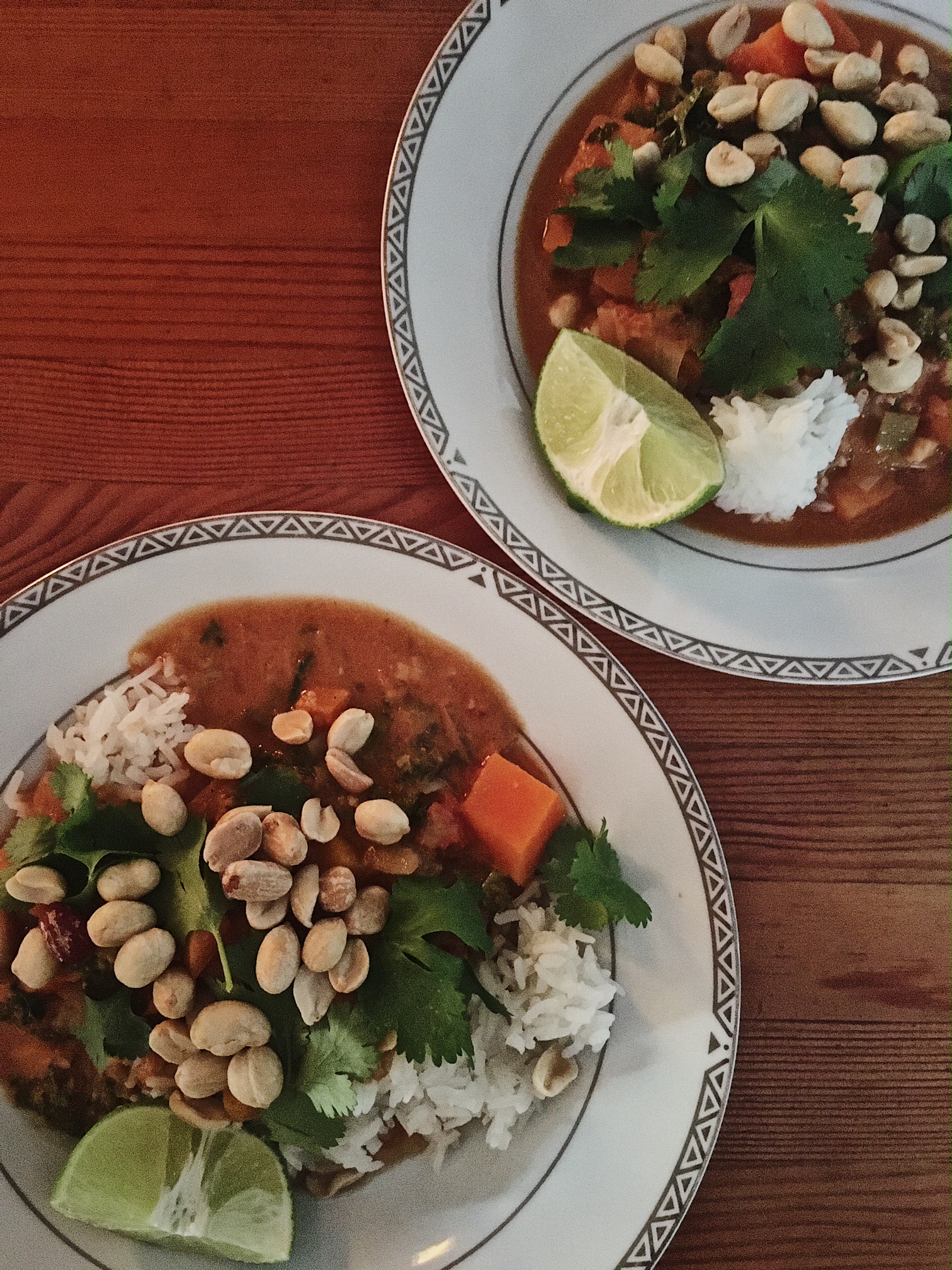 An overhead shot of a peanut stew served on white rise. The stew is topped with peanuts and cilantro. There's a wedge of lime on the side.
